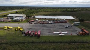 Vista aérea de uma base de combate a incêndios, com aviões, caminhões e equipes de emergência mobilizadas.