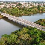 Vista aérea de uma ponte sobre um rio cercado por vegetação em Cuiabá, Mato Grosso.