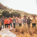 Grupo diverso de agricultores reunido em um campo iluminado pelo sol.