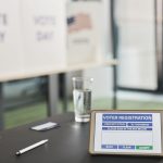 Tablet exibindo um cadastro eleitoral em uma estação de votação interna, com sinalização sobre o dia da votação.