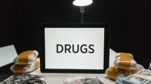 Drogas, dinheiro e algemas sobre uma mesa, em uma imagem ilustrativa sobre apreensão policial.